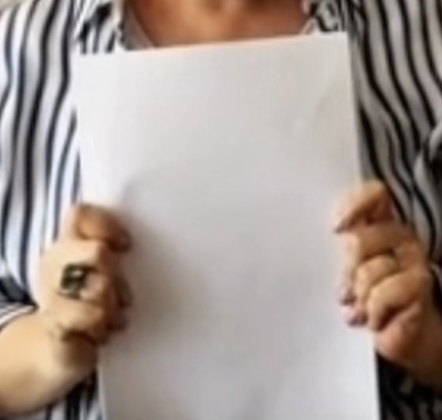 A person in a striped shirt holding a blank white sheet, with a large ring visible on one hand.